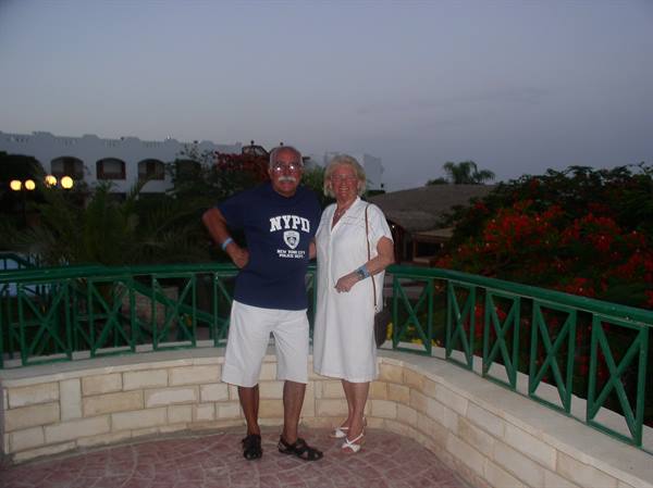 Couple posing beside a green railing on light stone, flowering trees behind