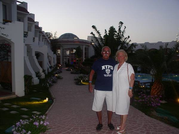Elderly couple on a resort walkway, white buildings and palms at dusk