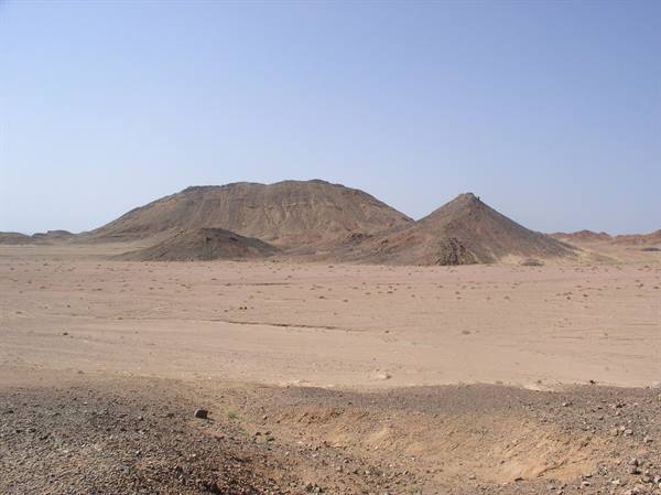 Brown rocky hills rising from sandy desert under clear blue sky