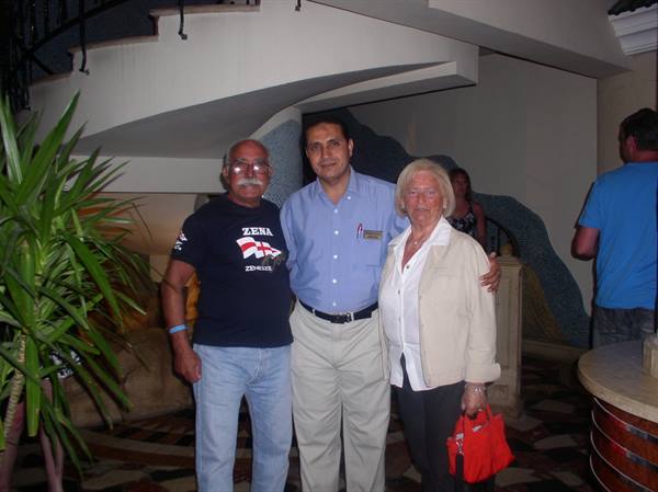 Elderly couple posing with hotel staff by spiral staircase in lobby
