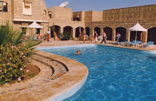 Sandstone pool with tourists, sun umbrellas and palms, Arabian arches
