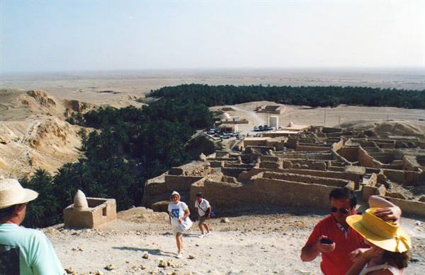 Tourists descend from earthen Berber village above Chenini oasis with palm groves