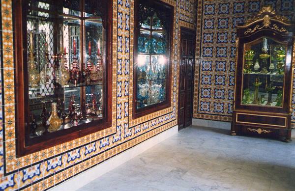 Glass display cases with colored bottles, carved wooden furniture, patterned tiled walls