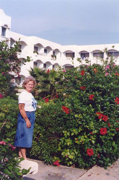 Woman among red hibiscus flowers in front of a white arched hotel