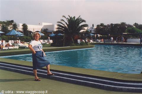 Woman in blue skirt by the pool with palm tree and umbrellas, daylight