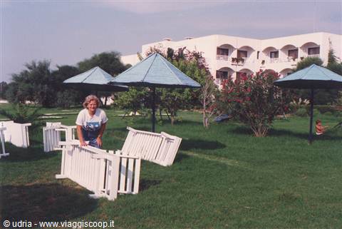 Smiling woman gathers blue parasols on the lawn in front of a white hotel