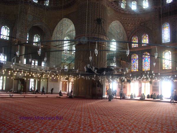 Inside the Blue Mosque, hanging lamps, red carpet and seated visitors