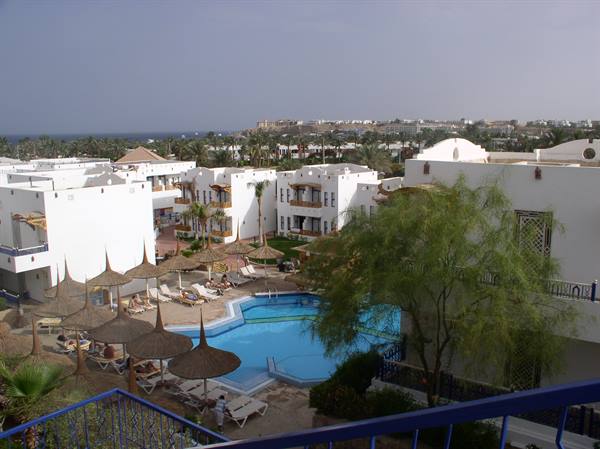 Blue pool with straw umbrellas, lounge chairs and white hotels by the Red Sea