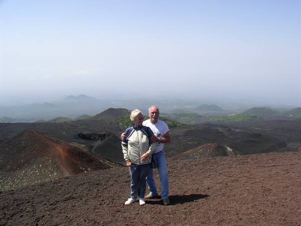 Elderly couple embracing on dark volcanic sand slope, craters in the background