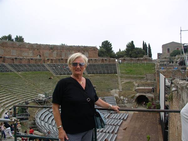 Blonde woman wearing sunglasses beside the ancient stone tiers of Taormina's Greek Theatre