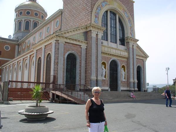 Woman in black top in front of Tindari sanctuary, brick facade with mosaics
