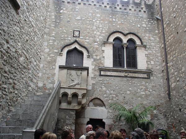 Tourists in the stone courtyard of Palazzo Corvaja in Taormina, Gothic mullioned window