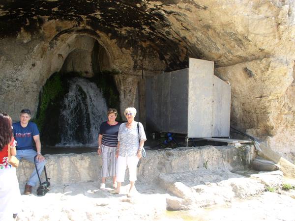 Tourists pose in front of a spring flowing from a rocky grotto
