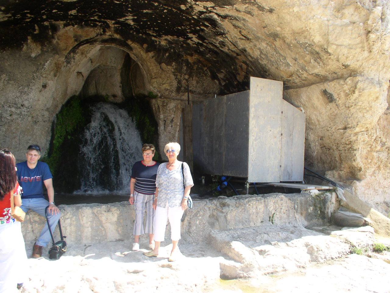 Tourists pose in front of a spring flowing from a rocky grotto