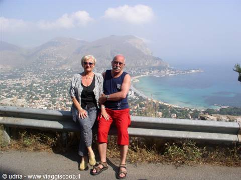 Couple leaning on guardrail above Mondello bay, mountain and beach behind