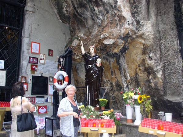 Saint statue in rock cave with red candles, flowers and votive offerings