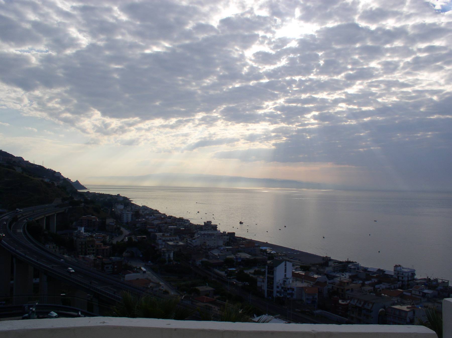 Sunbeams through clouds over the sea and coastal town, highway viaduct below