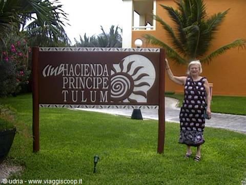 Woman beside the wooden Hacienda Principe Tulum sign, among palm trees and green lawn