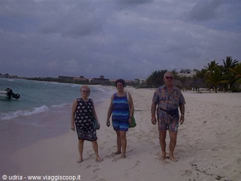 Three tourists walk barefoot on white sand, palms and a boat by the sea