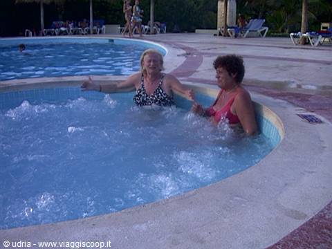Two women laughing in a round whirlpool spa beside a resort pool