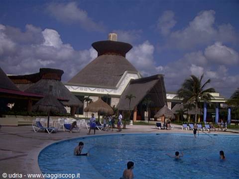 Swimmers in pool surrounded by thatched palapas and large cone-shaped building