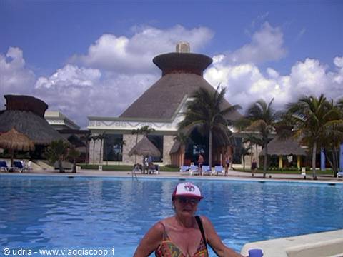 Woman in swimsuit by the pool, behind a volcano-shaped thatched building with palm trees