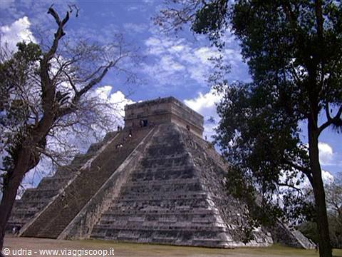 Kukulkan Pyramid at Chichen Itza framed by trees under a blue sky