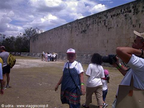 Tourists walk beside the massive stone wall of the Great Ball Court, Chichén Itzá