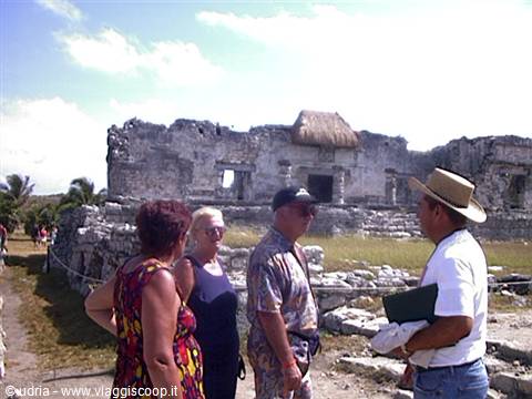 Tourists listen to the guide beside ancient Maya stone ruins