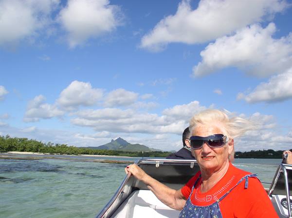 Woman with sunglasses on a boat, mountain on the coast behind