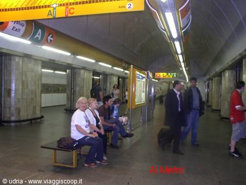 Travelers seated waiting in a metro station with marble pillars and bright lights