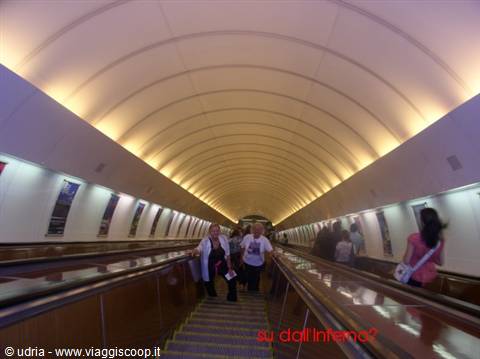 Tourists on long escalators inside a curved illuminated metro tunnel