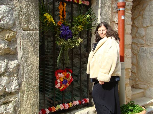 Woman in cream fur coat beside an iron-gated door decorated with colorful flowers