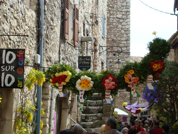 Floral decorations hang between stone houses, crowd in a medieval alley