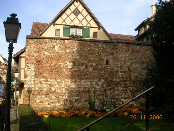 Half-timbered house behind old stone wall with colorful flowers, daylight