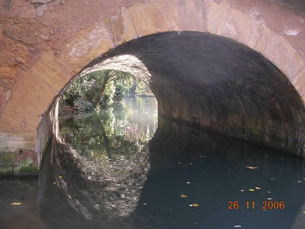 Stone bridge arch reflected in canal water with floating leaves
