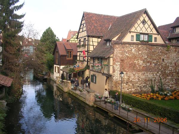 Half-timbered houses along a canal in Colmar, people on a wooden footbridge