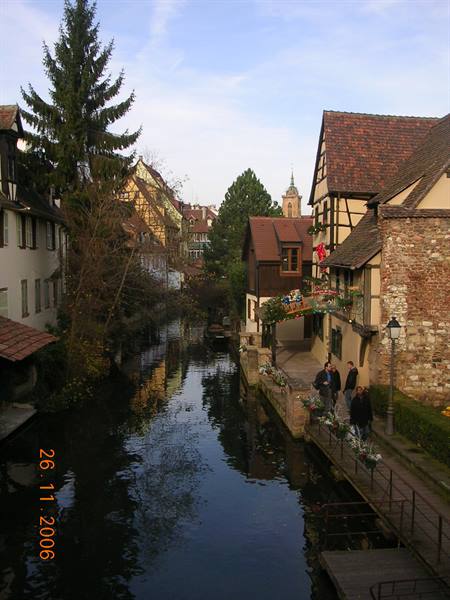 Timbered houses along a canal in Colmar, people strolling on wooden footbridge
