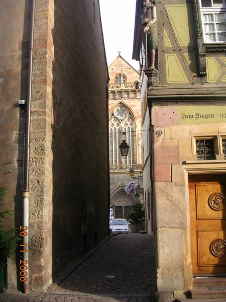 Cobbled alley with half-timbered facade and statue, gothic church beyond