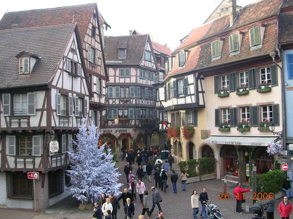 Half-timbered houses on cobbled square, white decorated Christmas tree, people strolling