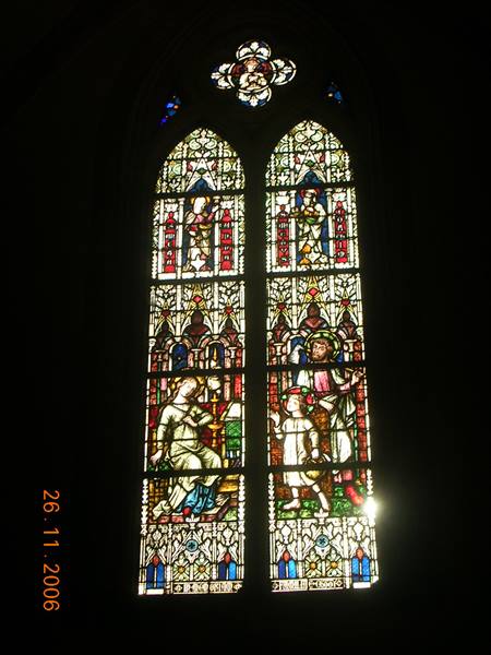 Gothic stained glass window with religious scenes, sunlight in dark church