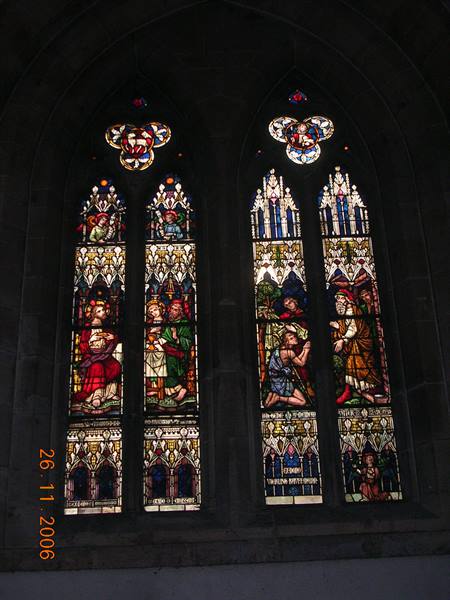 Gothic stained glass windows with sacred figures, light filtering through colored glass
