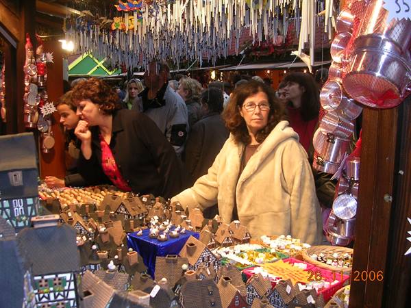 Woman in fur coat browses wooden houses at crowded Christmas market