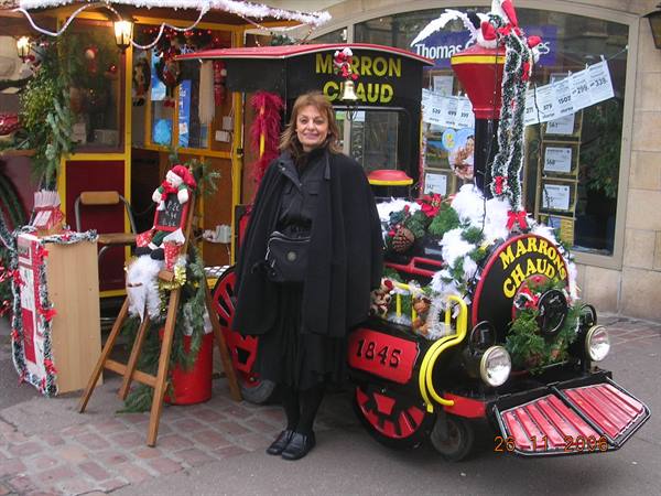 Woman in black beside a small Christmas locomotive, festive decorated shop windows