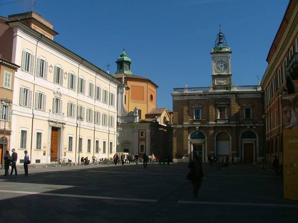 Piazza Tre Martiri in Rimini, people walking by the clock-topped palace