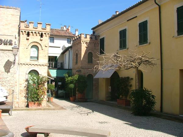 Cobbled little square with yellow houses, crenellated brick buildings and potted plants