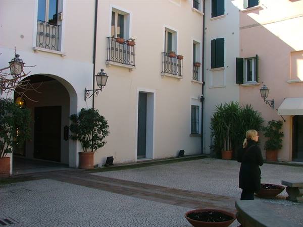 Woman in cobbled courtyard among pastel buildings with flowered balconies and lanterns