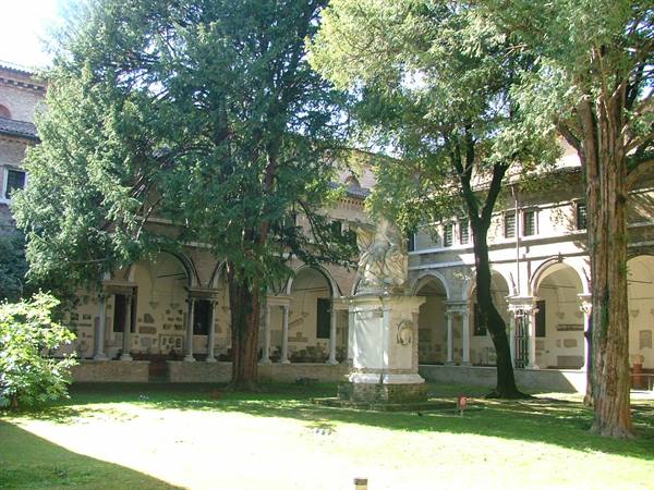 Stone-arched cloister with tall green trees and a marble statue on pedestal