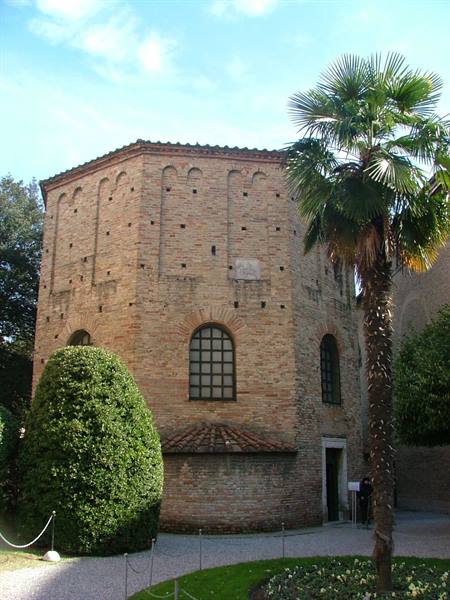 Neonian Baptistery in Ravenna, ancient brick walls, palm tree and hedge under blue sky