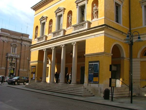 Yellow facade of the Teatro Alighieri in Ravenna, with columns, statues and passersby